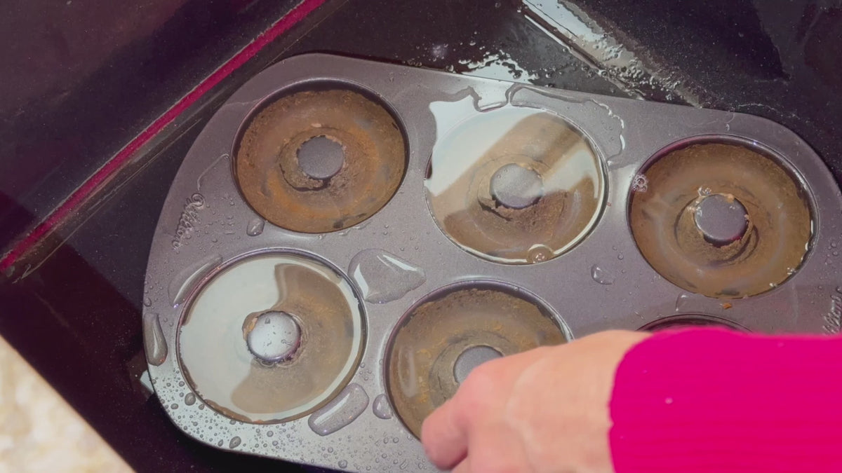 Load video: Swishy cleaning sponge removing baked-on residue from a donut pan